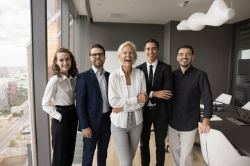 Wall Mural - Cheerful excited business team office front portrait. Happy senior business leader woman and younger colleagues looking at camera, smiling, laughing, celebrating success, work achievement