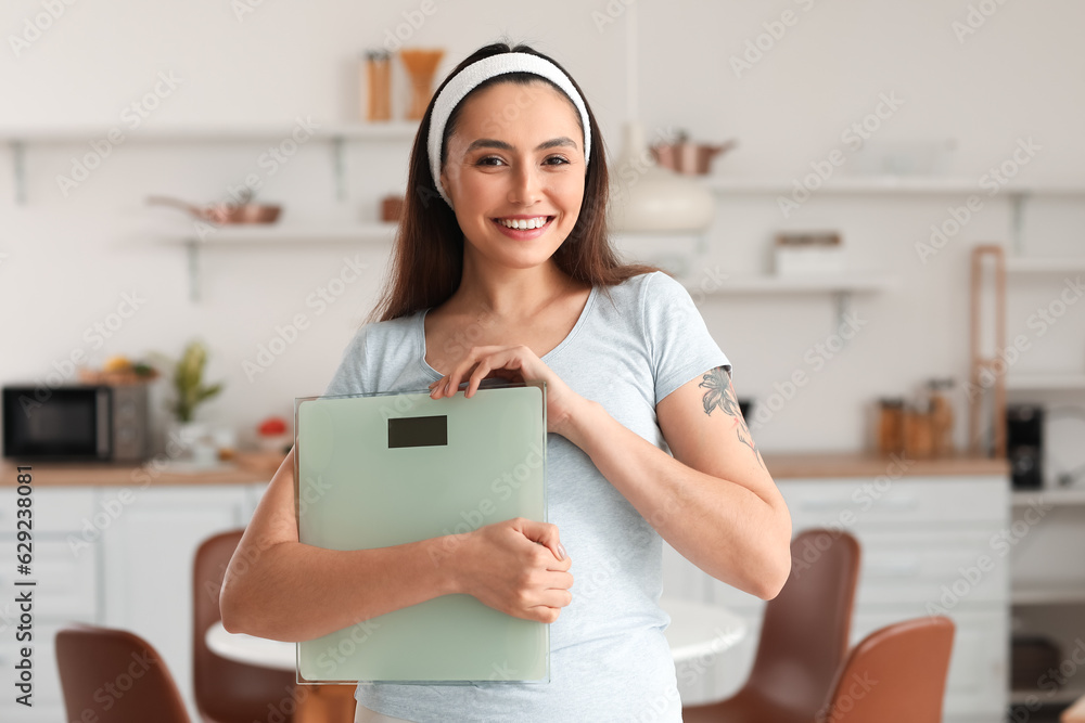 Sporty young woman with scales in kitchen