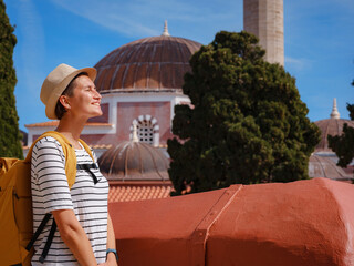 summer trip to Rhodes island Greece. Young Asian woman in striped tshirt and hat walks Street of Knights of Fortifications castle. female traveler visiting southern Europe. Unesco world heritage site