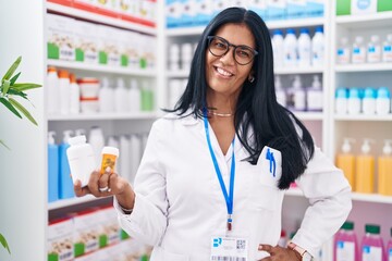 Wall Mural - Middle age hispanic woman pharmacist smiling confident holding pills bottles at pharmacy