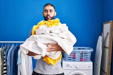 Poster - Middle east man with beard holding pile of laundry making fish face with mouth and squinting eyes, crazy and comical.