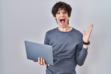 Poster - Young man working using computer laptop celebrating victory with happy smile and winner expression with raised hands