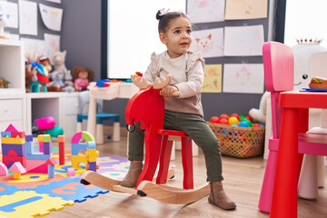 Wall Mural - Adorable hispanic girl playing with reindeer rocking at kindergarten