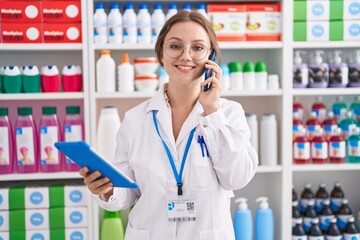 Sticker - Young blonde woman pharmacist using touchpad talking on smartphone at pharmacy