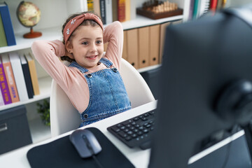 Adorable hispanic girl student using computer relaxed with hands on head at classroom