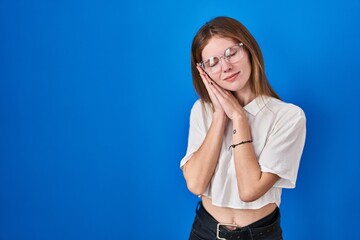 Sticker - Beautiful woman standing over blue background sleeping tired dreaming and posing with hands together while smiling with closed eyes.