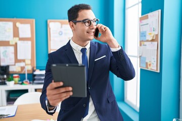 Sticker - Young hispanic man business worker talkiong on smartphone using touchpad at office