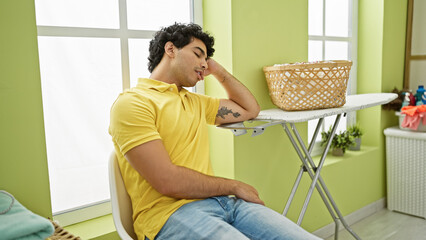 Sticker - Young latin man waiting for washing machine sitting on chair sleeping at laundry room