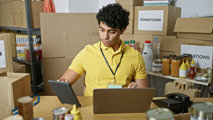 Wall Mural - Young latin man volunteer using laptop and touchpad sitting on table at charity center