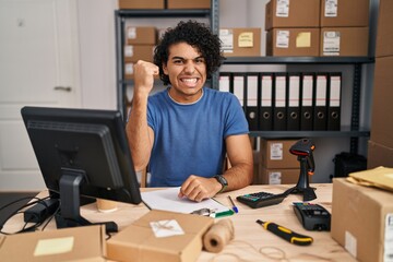 Canvas Print - Hispanic man with curly hair working at small business ecommerce angry and mad raising fist frustrated and furious while shouting with anger. rage and aggressive concept.