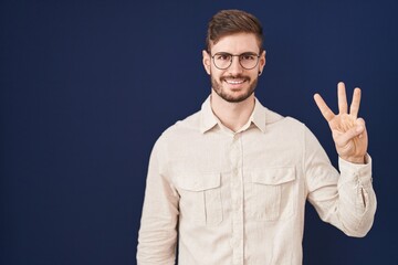 Poster - Hispanic man with beard standing over blue background showing and pointing up with fingers number three while smiling confident and happy.