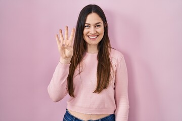 Canvas Print - Young brunette woman standing over pink background showing and pointing up with fingers number four while smiling confident and happy.