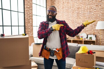 Sticker - African american man working at home renovation amazed and smiling to the camera while presenting with hand and pointing with finger.