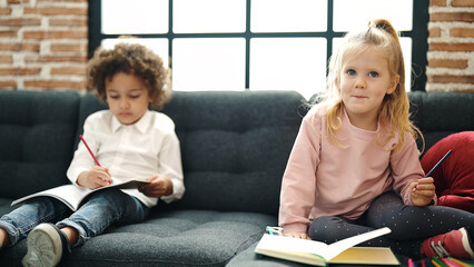 Sticker - Adorable boy and girl students sitting on sofa drawing on notebook at home