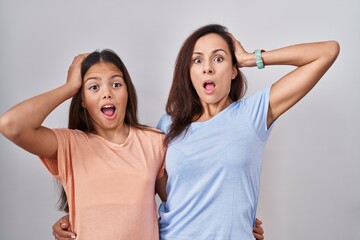 Poster - Young mother and daughter standing over white background crazy and scared with hands on head, afraid and surprised of shock with open mouth