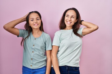 Wall Mural - Young mother and daughter standing over pink background smiling confident touching hair with hand up gesture, posing attractive and fashionable