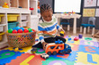 African american boy playing with car toy sitting on floor at kindergarten