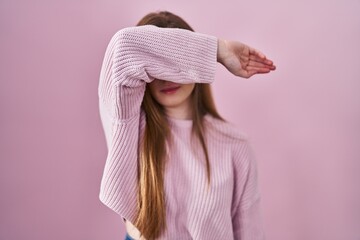 Poster - Young caucasian woman standing over pink background covering eyes with arm, looking serious and sad. sightless, hiding and rejection concept