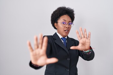 Canvas Print - Beautiful african woman with curly hair wearing business jacket and glasses afraid and terrified with fear expression stop gesture with hands, shouting in shock. panic concept.