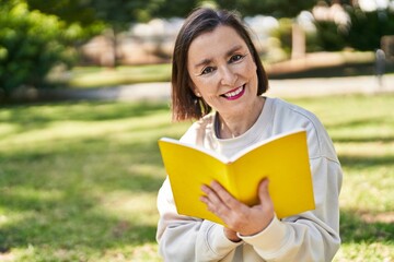 Wall Mural - Middle age woman reading book sitting on herb at park