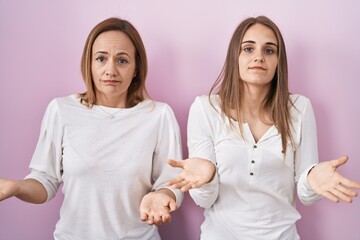 Sticker - Middle age mother and young daughter standing over pink background clueless and confused with open arms, no idea concept.