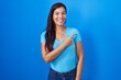 © Krakenimages.com - Young hispanic woman standing over blue background cheerful with a smile of face pointing with hand and finger up to the side with happy and natural expression on face