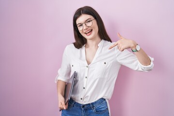 Sticker - Young caucasian woman holding laptop looking confident with smile on face, pointing oneself with fingers proud and happy.