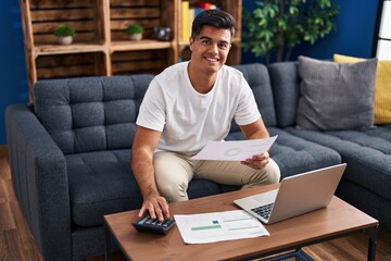 Sticker - Young hispanic man using laptop reading document accounting at home