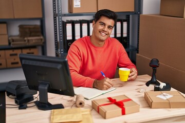 Poster - Young hispanic man ecommerce business worker writing on notebook drinking coffee at office