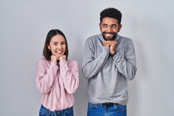 Poster - Young hispanic couple standing together laughing nervous and excited with hands on chin looking to the side