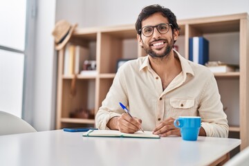 Sticker - Young hispanic man writing on notebook at home