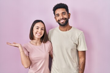 Sticker - Young hispanic couple together over pink background pointing aside with hands open palms showing copy space, presenting advertisement smiling excited happy