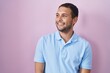 © Krakenimages.com - Hispanic man standing over pink background looking away to side with smile on face, natural expression. laughing confident.