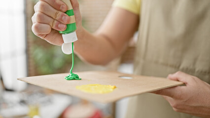 Young hispanic man artist pouring color on palette at art studio