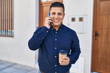 Wall Mural - Young latin man talking on smartphone drinking coffee at street