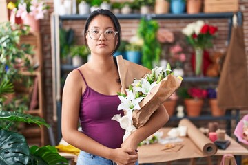 Canvas Print - Asian young woman at florist shop holding bouquet of flowers thinking attitude and sober expression looking self confident