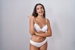 © Krakenimages.com - Young hispanic woman wearing white lingerie smiling with happy face looking and pointing to the side with thumb up.