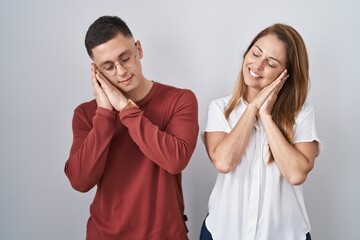 Wall Mural - Mother and son standing together over isolated background sleeping tired dreaming and posing with hands together while smiling with closed eyes.