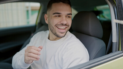 Sticker - Young hispanic man smiling confident sitting on car at street