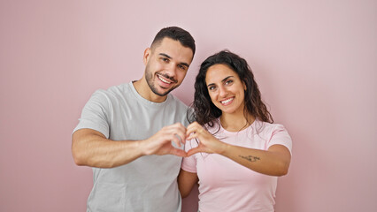 man and woman couple doing heart gesture smiling over isolated pink background