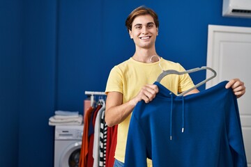 Wall Mural - Young caucasian man smiling confident putting sweatshirt on hanger at laundry room