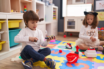 Adorable boy and girl playing supermarket game sitting on floor at kindergarten