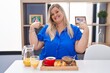 © Krakenimages.com - Caucasian plus size woman eating breakfast at home looking confident with smile on face, pointing oneself with fingers proud and happy.