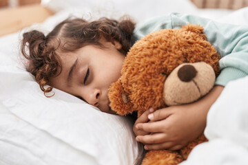 Adorable hispanic girl hugging teddy bear lying on bed sleeping at bedroom