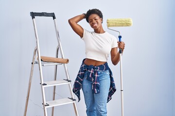 Poster - African american woman holding roller painter smiling confident touching hair with hand up gesture, posing attractive and fashionable