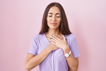 Sticker - Young hispanic woman with long hair standing over pink background smiling with hands on chest with closed eyes and grateful gesture on face. health concept.