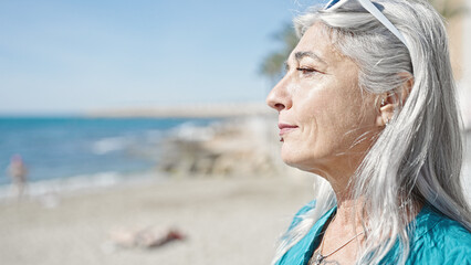 Poster - Middle age grey-haired woman standing with relaxed expression at beach