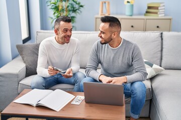 Two men using laptop counting dollars at home