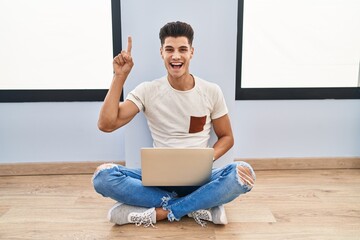 Sticker - Young hispanic man using laptop at home smiling amazed and surprised and pointing up with fingers and raised arms.