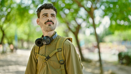 Wall Mural - Young hispanic man tourist wearing backpack and headphones at park